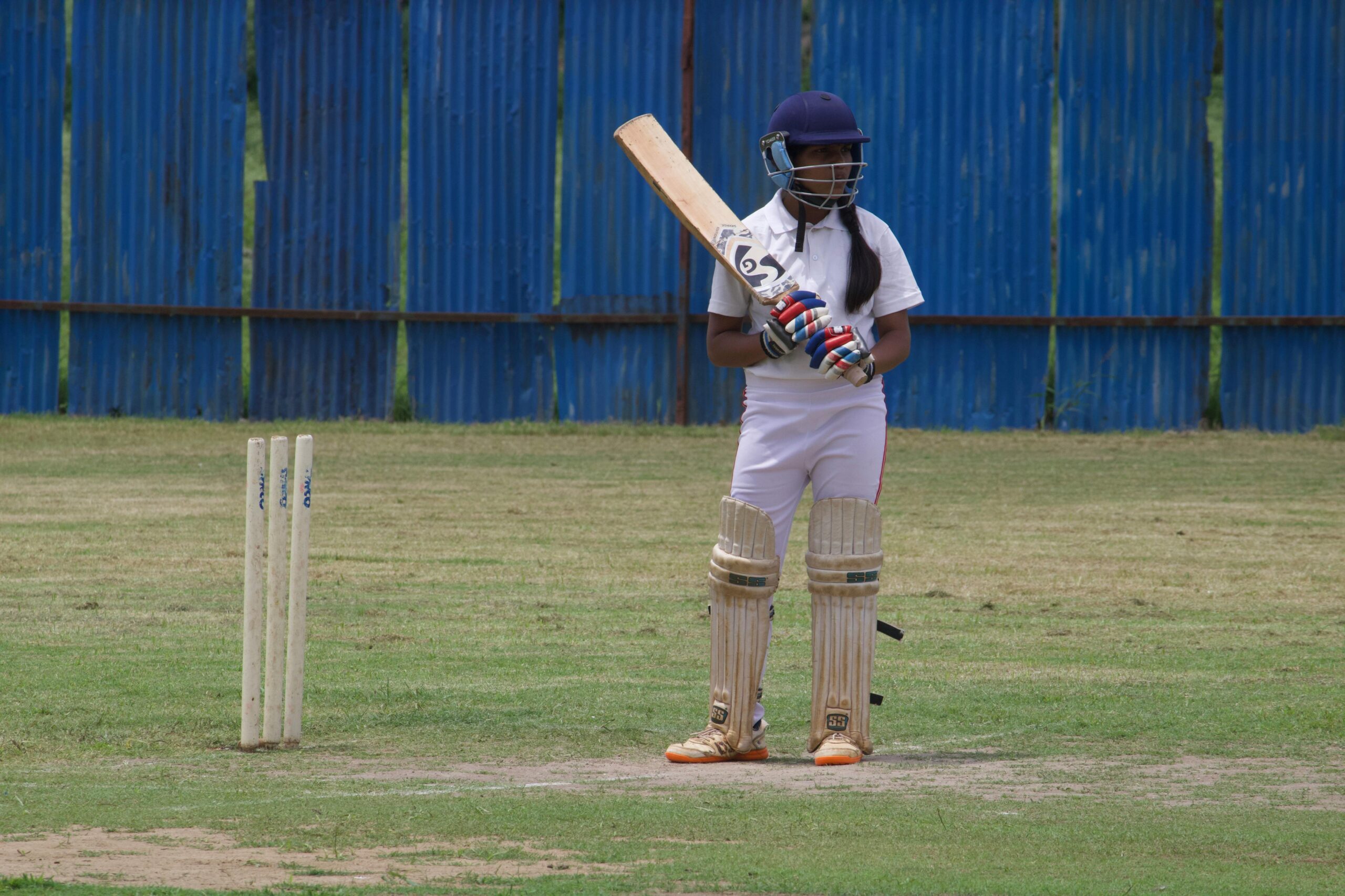 A young female cricket player poised to bat on a grassy field in Gahunje, India.